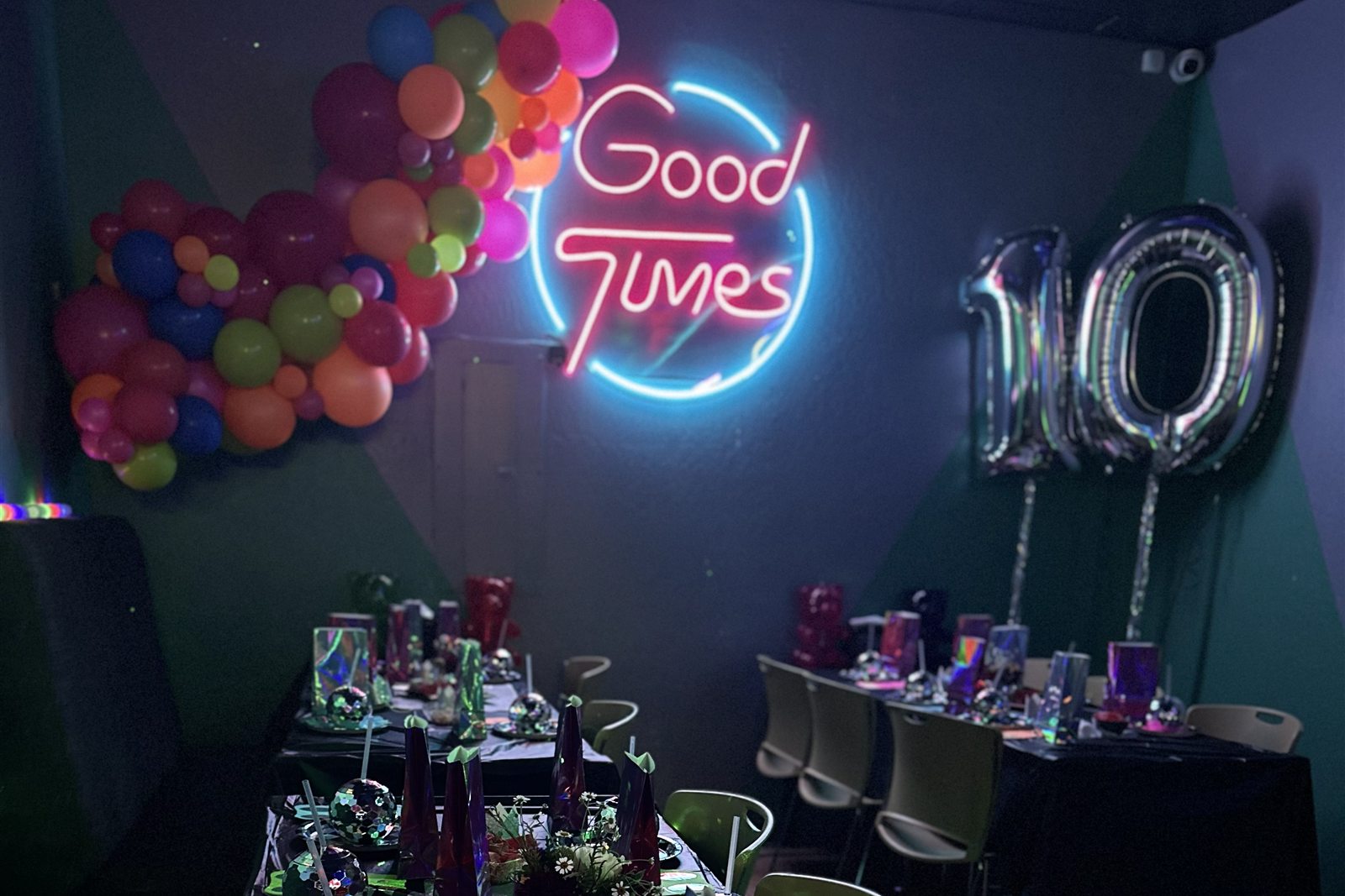 The party room set up for a 10th birthday, with a balloon garland, silver number balloons, and decorated tables under the Good Times neon sign
